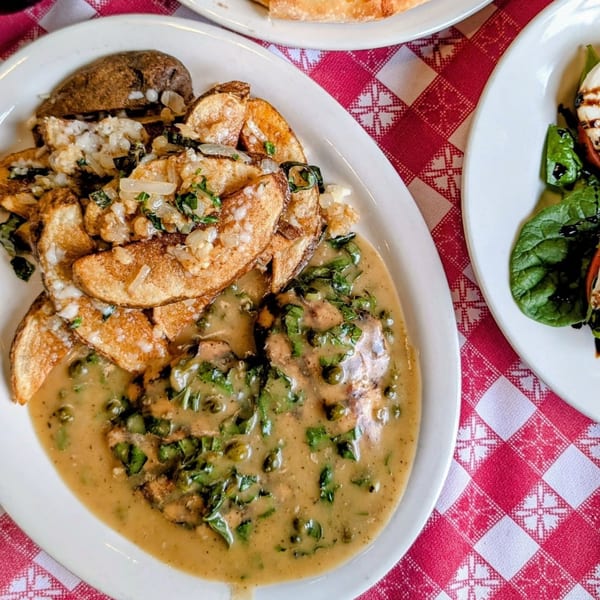 Italian chicken piccata with capers, parsley, and roasted potatoes on a red and white checkered tablecloth.