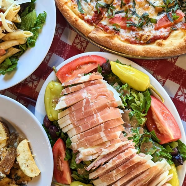 A Margherita pizza, pasta salad, and a large Italian salad with prosciutto and mozzarella.