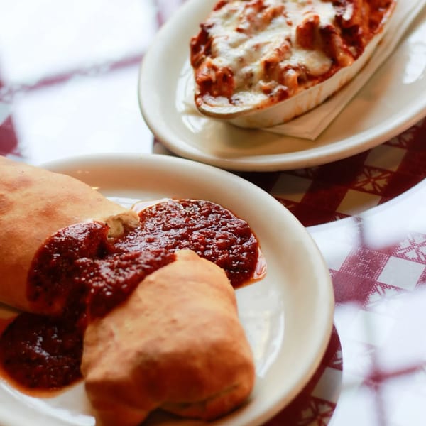 Calzone with marinara sauce and a baked pasta dish on a red and white checkered tablecloth.