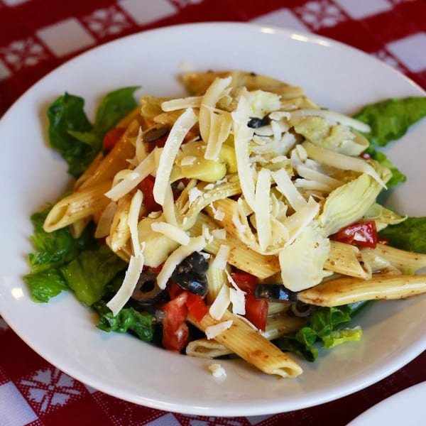 Penne pasta salad with lettuce, tomatoes, black olives, artichoke hearts, and shredded cheese.