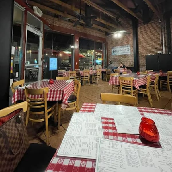 Interior of The Kitchen Italian Cafe & Pizzeria with red and white checkered tablecloths and brick walls.