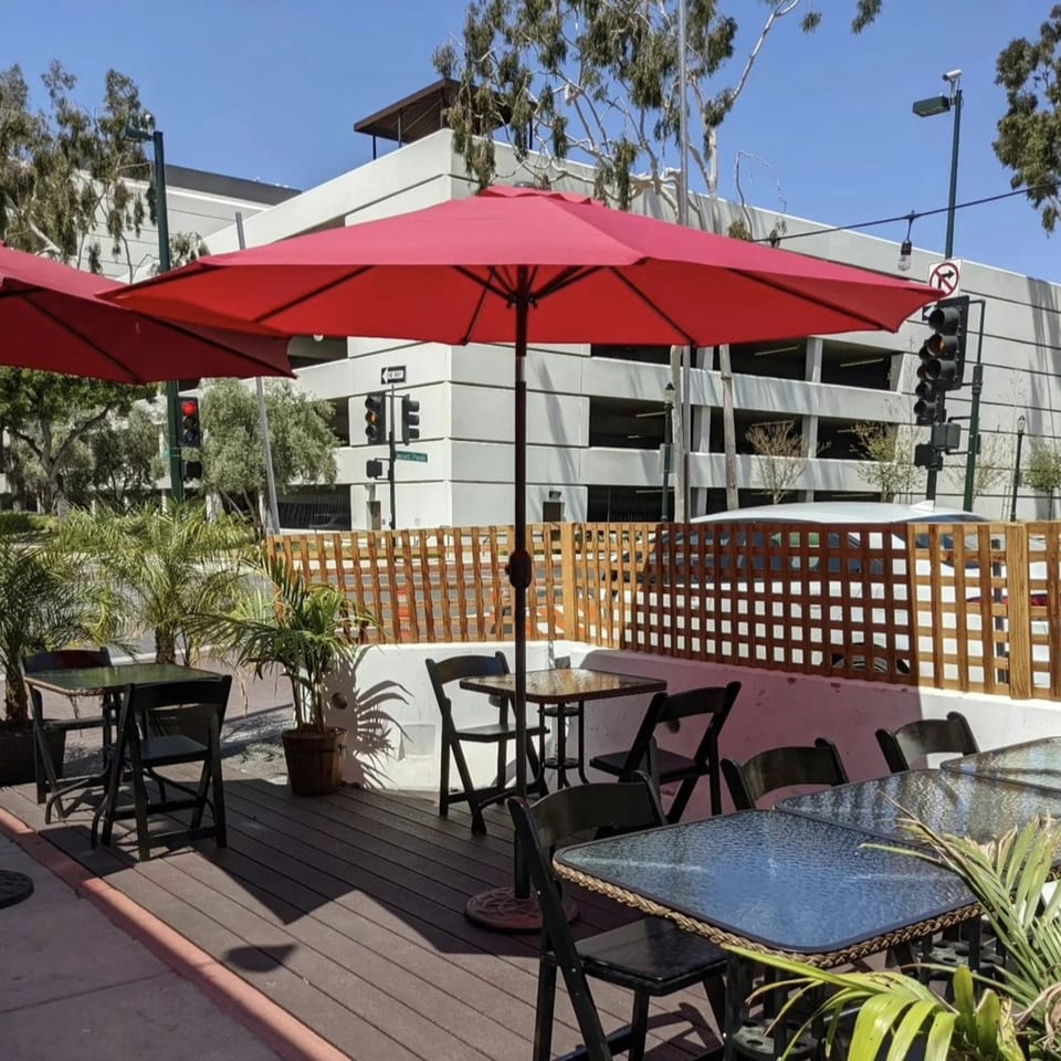 Outdoor patio of The Kitchen Italian Cafe & Pizzeria with red umbrellas, tables, and chairs.