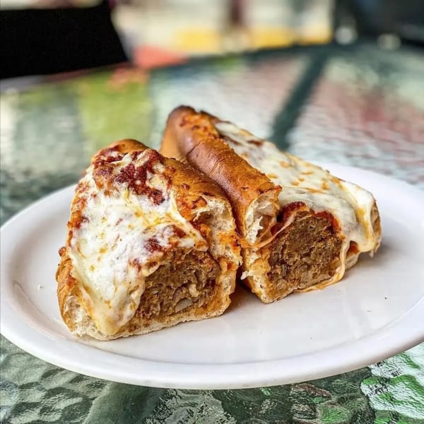 Two halves of a meatball sub with melted mozzarella cheese and marinara sauce on a white plate.
