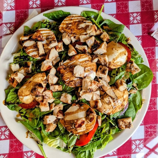 Italian salad with grilled chicken, mozzarella, tomatoes, and spinach on a red and white checkered tablecloth.