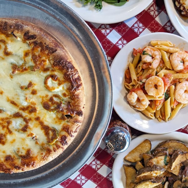 A calzone, shrimp penne pasta, and potato wedges on a red and white checkered tablecloth.